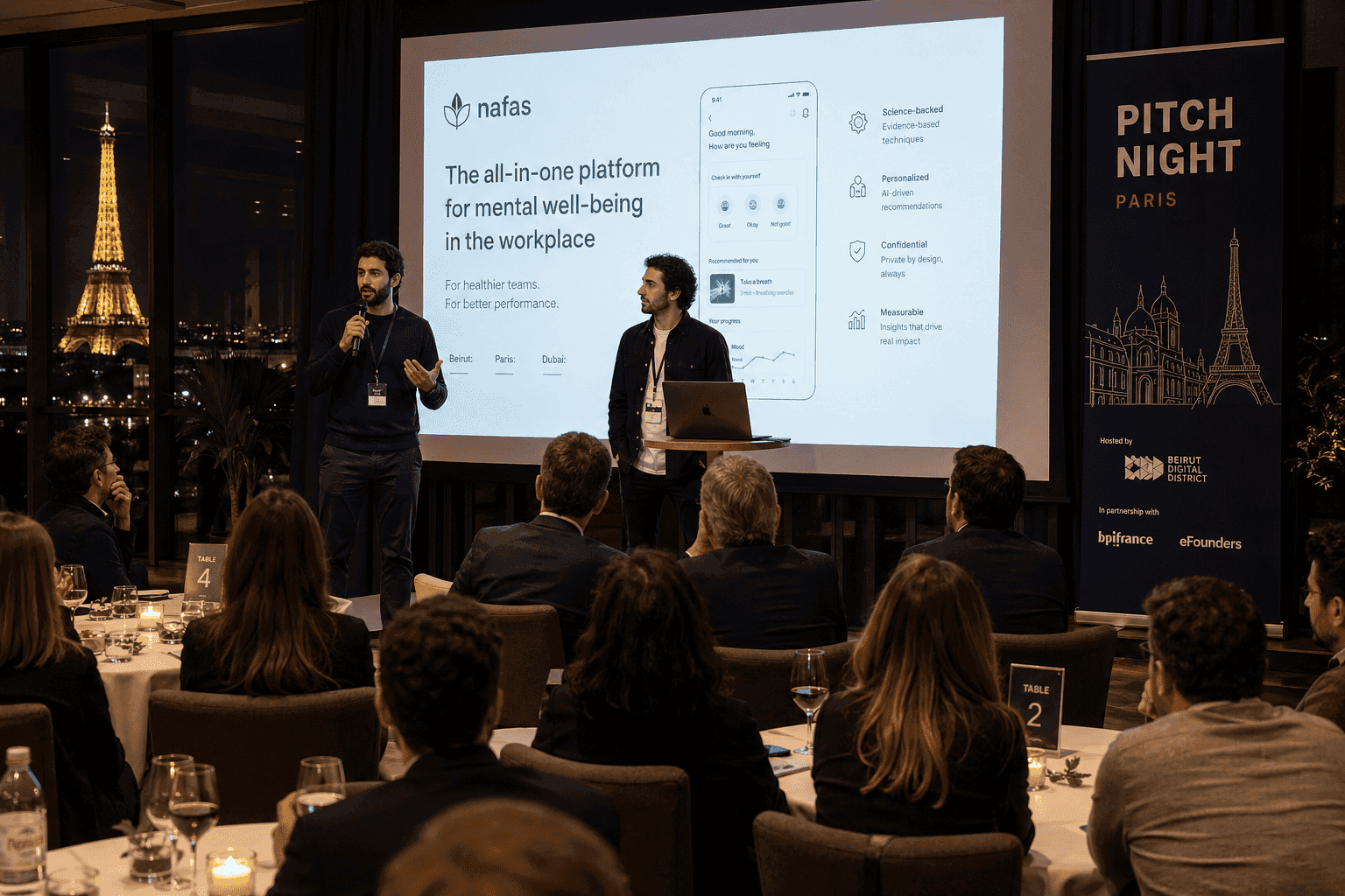 Lebanese founders presenting to a room of investors at an evening Pitch Night event in Paris, with a slide deck on screen and audience seated at round tables.