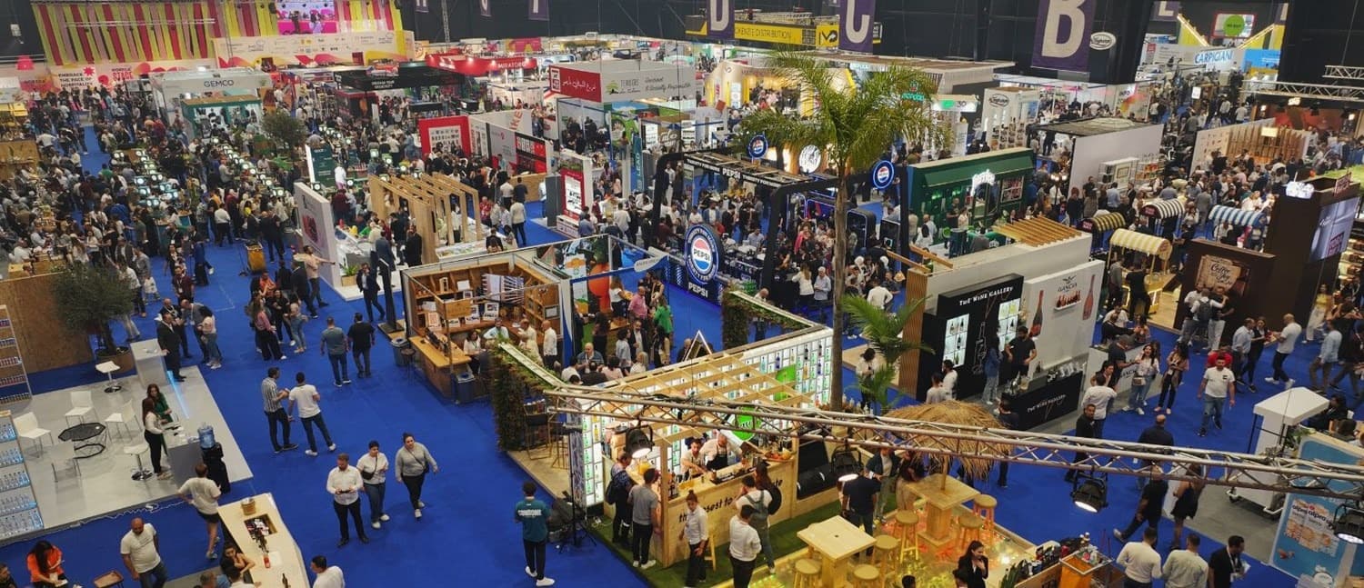 Wide shot of the HORECA Lebanon exhibition floor at Beirut's Seaside Arena, with professional visitors browsing food, beverage and equipment stands under bright overhead lighting.