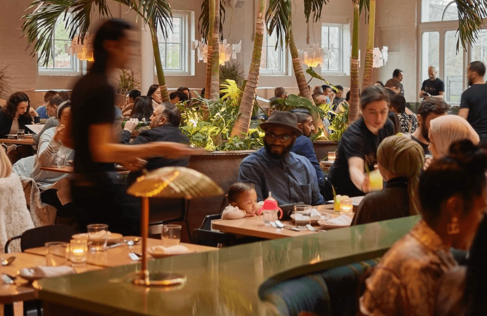 The dining room at Kalaya in Philadelphia, with tall indoor plants, wooden tables and warm lighting, co-owned by Lebanese entrepreneur Roland Kassis