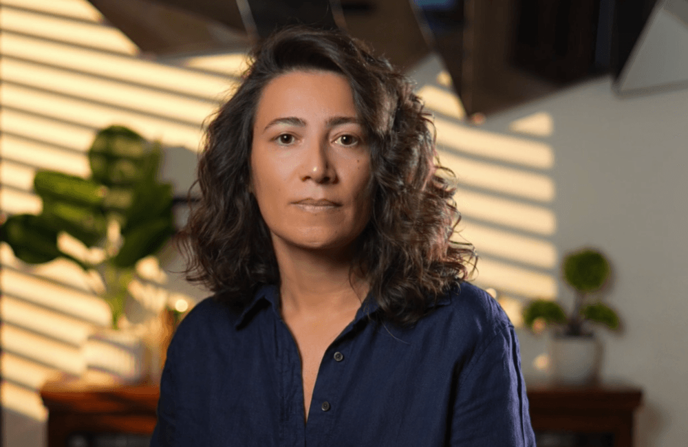 Jessy Shaanin, founder and CEO of SouqMetrics, in a dark blue shirt, photographed against a sunlit wall with plants behind.