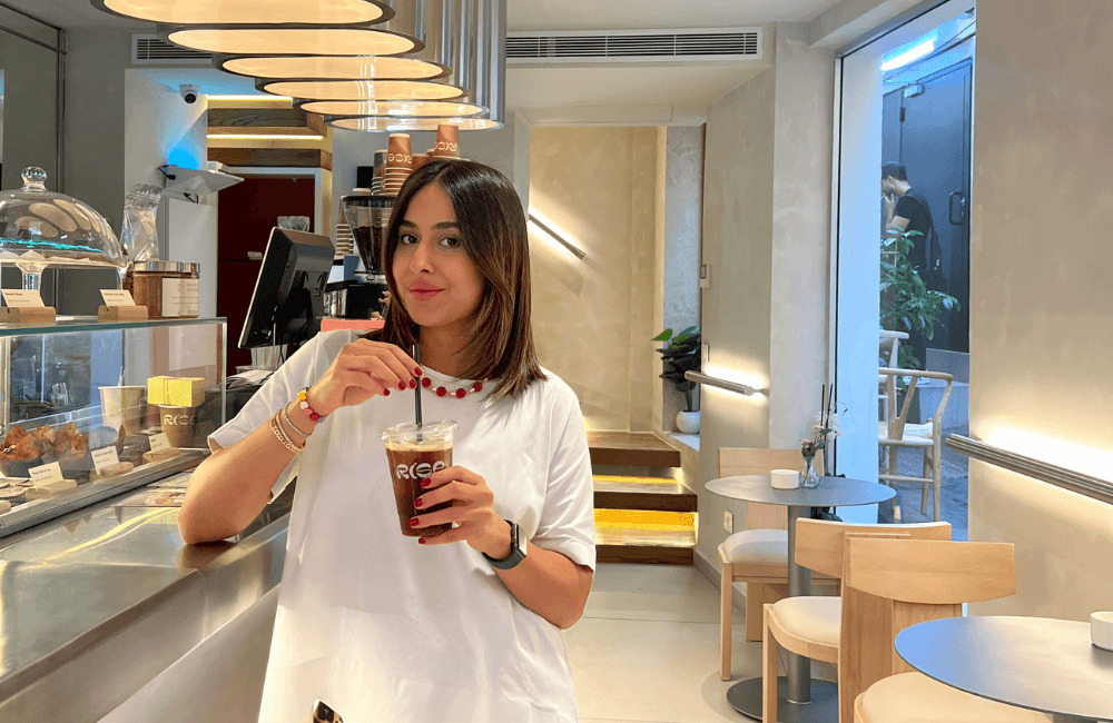 Rise founder Melissa El Haddad holding an iced coffee in a branded Rise cup at the counter of her cafe in Gemmayze, Beirut
