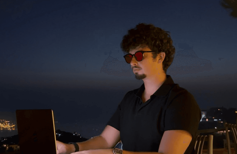 Souheil Sabban, founder of Viral Vision, working on a laptop at an outdoor terrace table at night, with city lights along the coast behind him.