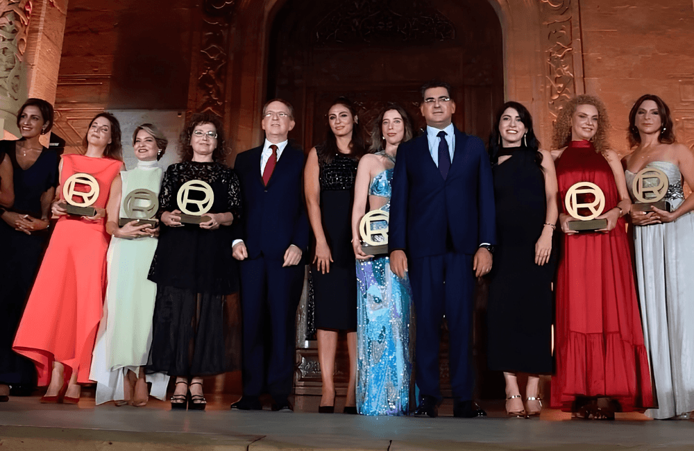 The six 2026 Women of Worth honourees hold gold trophies at the L'Oréal Paris ceremony, standing with guests in front of the stone archway of Résidence des Pins in Beirut.