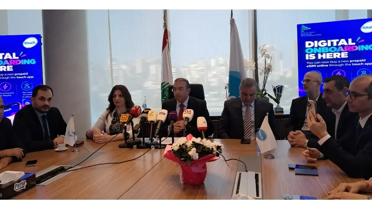 touch press conference launching its digital onboarding service, with officials seated around a wooden table, a cluster of TV microphones in front of the central speaker, Lebanese and touch flags behind them, and screens reading “Digital Onboarding Is Here” promoting prepaid eSIM sign up through the touch app