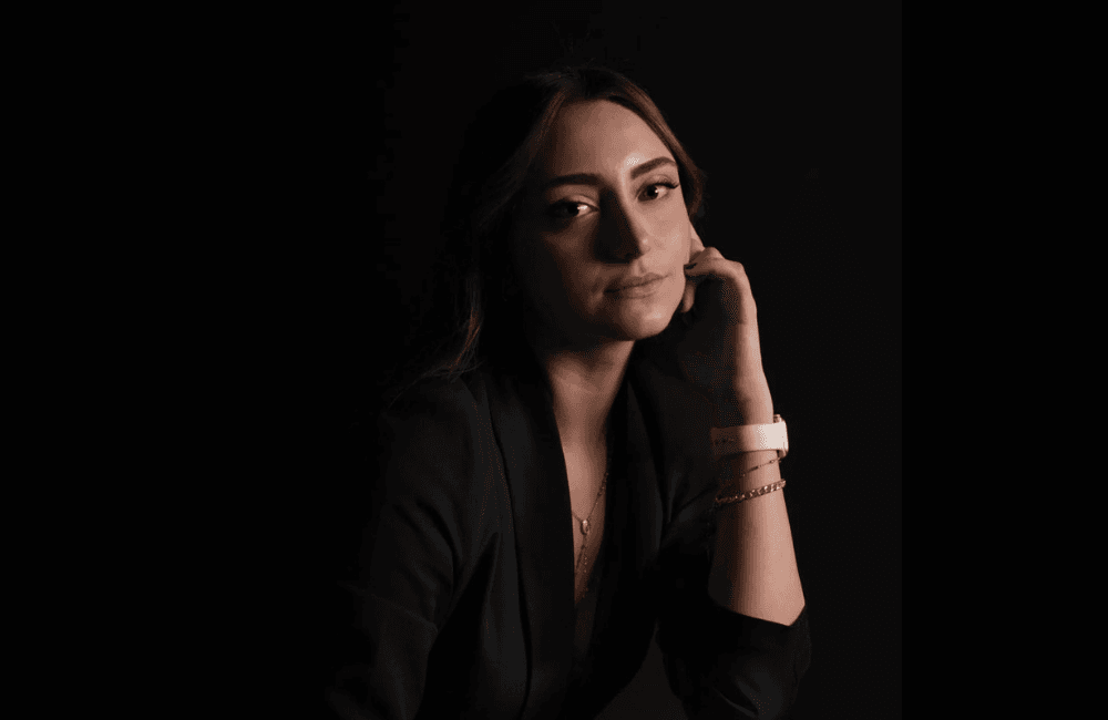 SevenPees founder and creative director Pia Takchi in a black blazer, resting her chin on her hand against a dark studio background